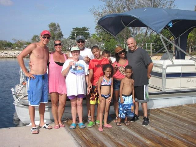 Stacey Sandlin Benas Veikalas Mortgage Broker Slam Dunk Mortgage Team Viera Melbourne Florida, family travels on dock by boat under blue sky, a wooden dock extending into calm water, with a group of people standing near a boat